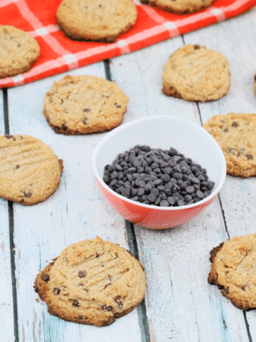 Gluten-free chocolate chip cookies made with almond flour on a white table with a bowl of chocolate chips in the middle of them