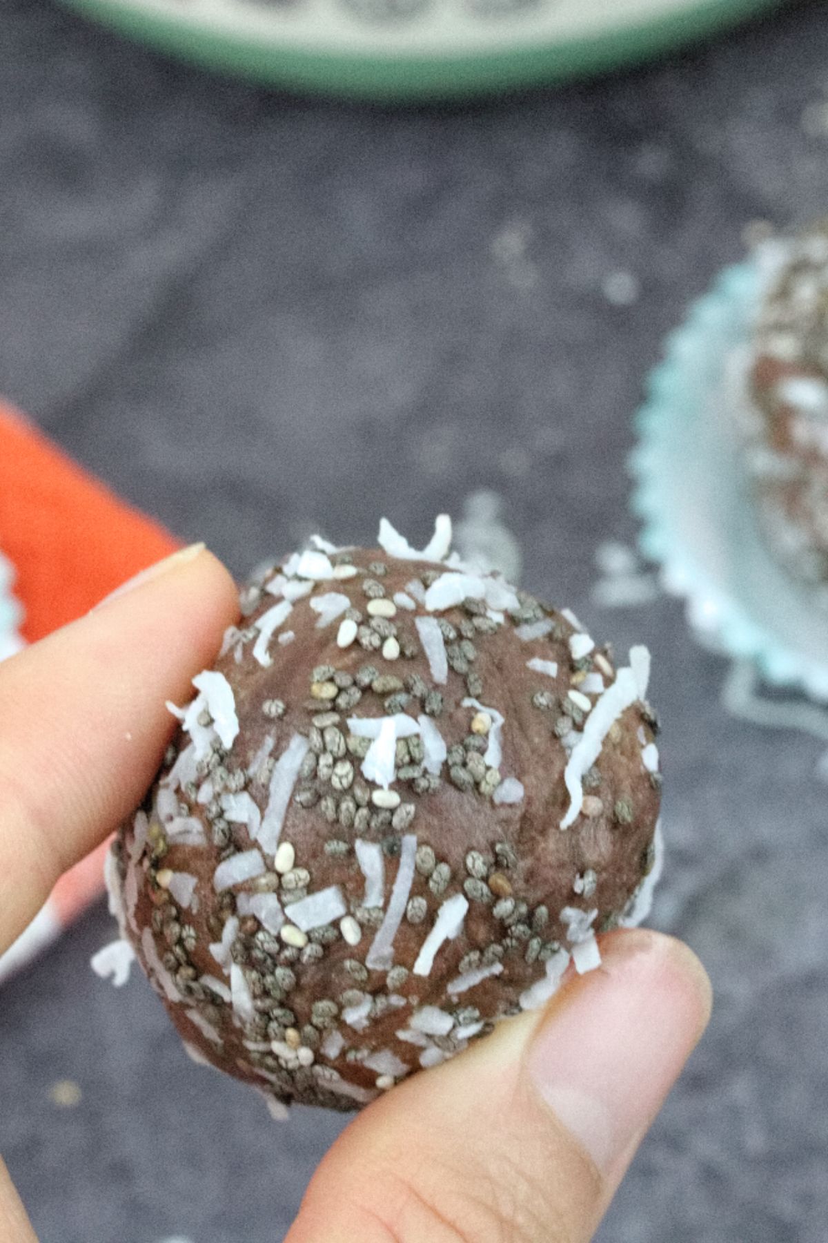 Two fingers holding up a chocolate protein ball coated in chia seeds.