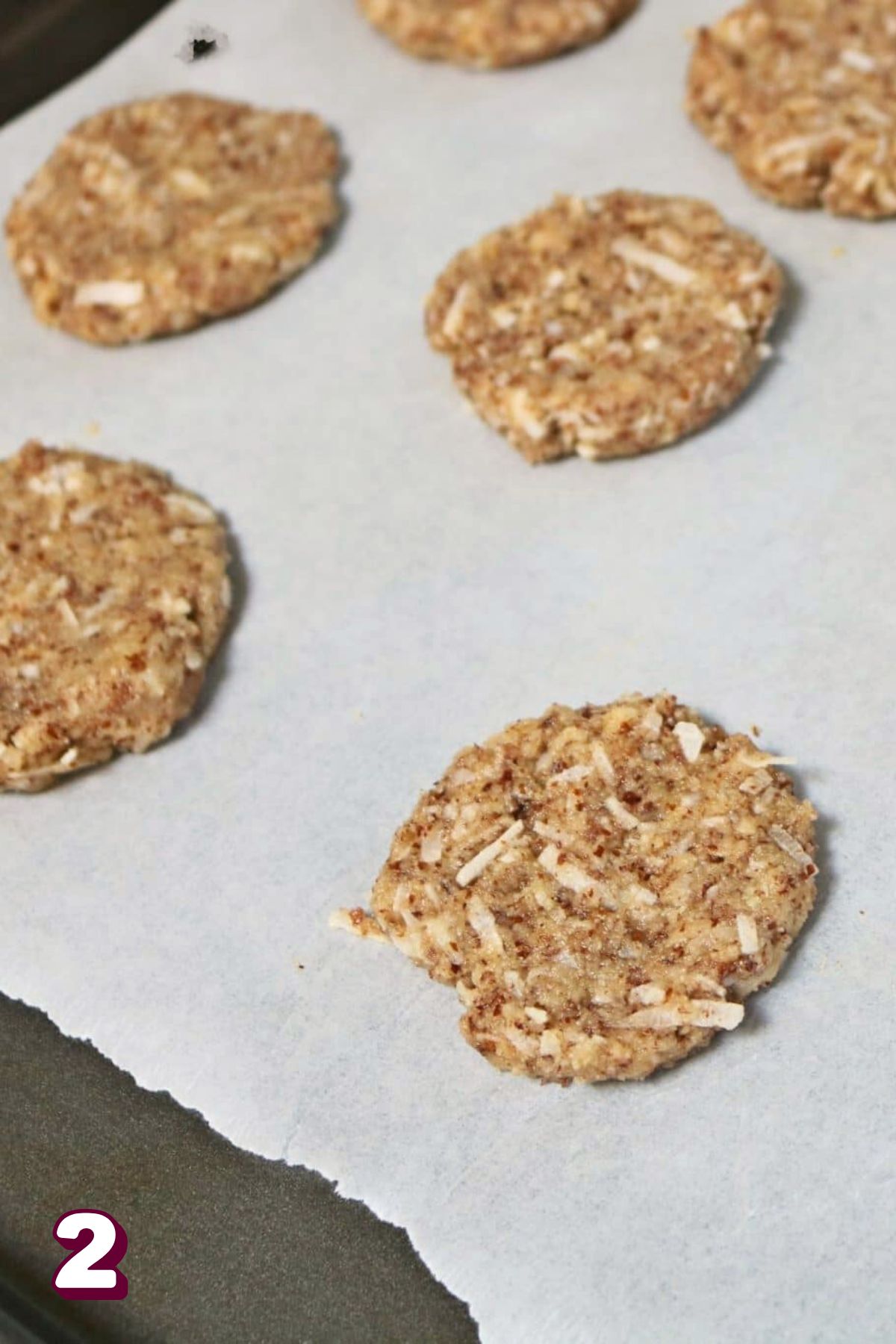 Almond and coconut cookies on a piece of parchment paper on a baking tray.