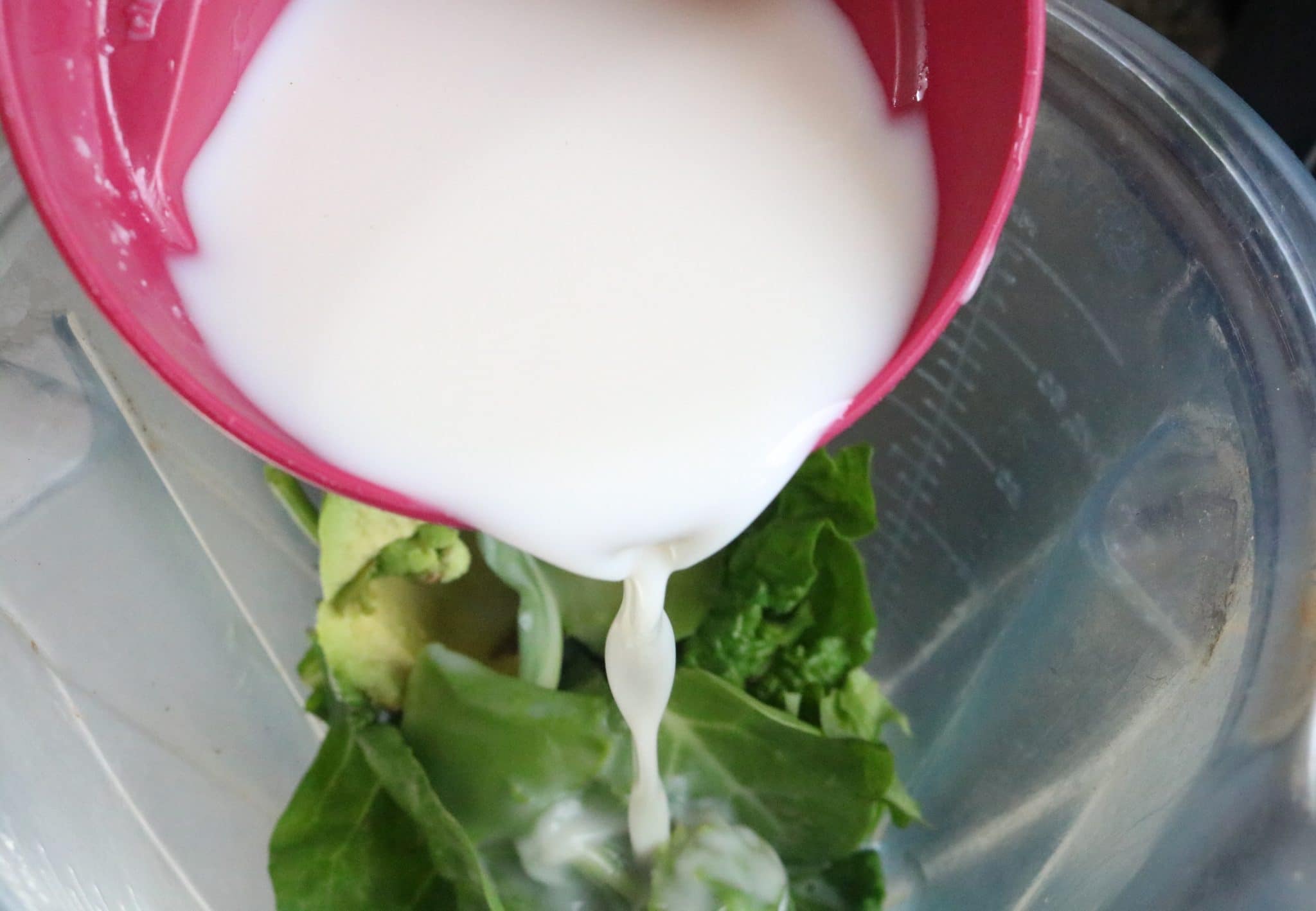 Hemp milk being poured into a blender with green smoothie ingredients