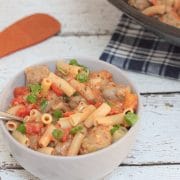 Tan bowl with tomato and sausage pasta on gluten-free rice noodles topped with green onions and spoon in the bowl