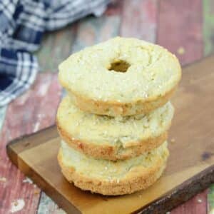 Three protein bagels stacked on a wooden cutting board with a blue linen begin it