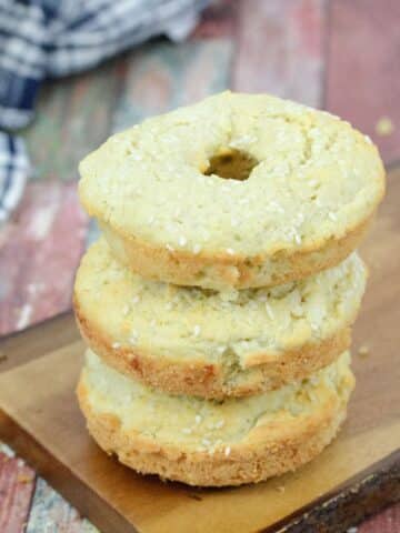 Three protein bagels stacked on a wooden cutting board with a blue linen begin it