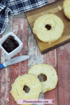 A sliced homemade bagel with another gluten-free bagel on a cutting board behind it and jam and a knife beside it