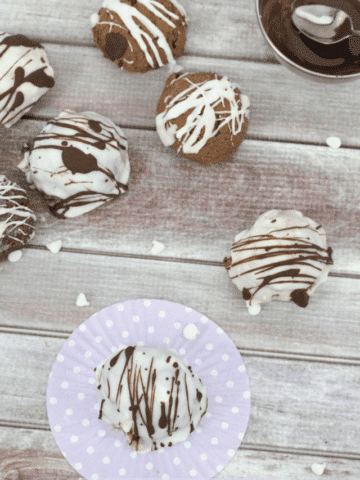 White chocolate coated zebra truffles scattered with one chocolate truffle on a purple muffin liner and white chocolate chips around them
