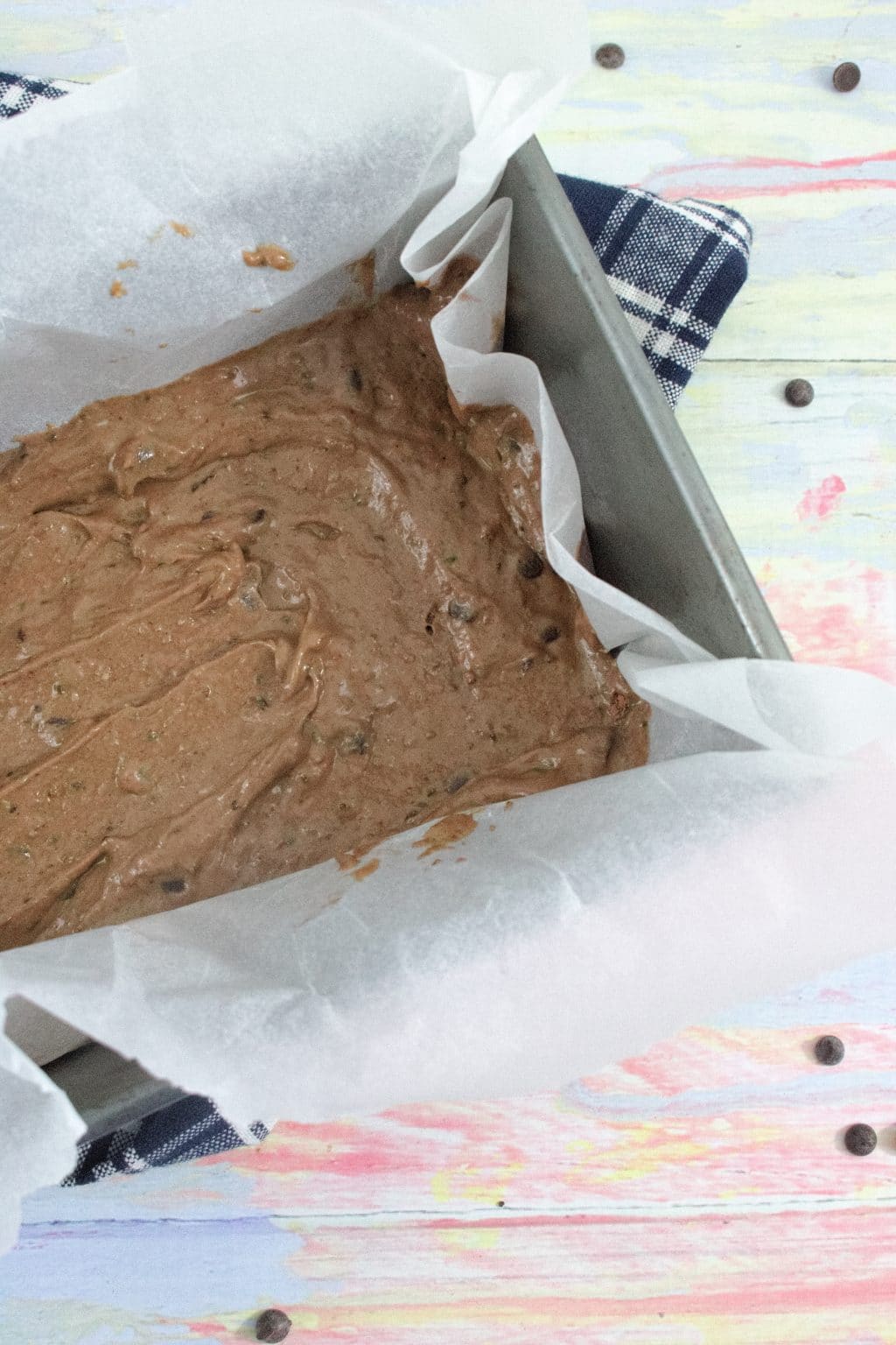 Baking tray lined with parchment paper filled with protein brownie mix all on a blue linen