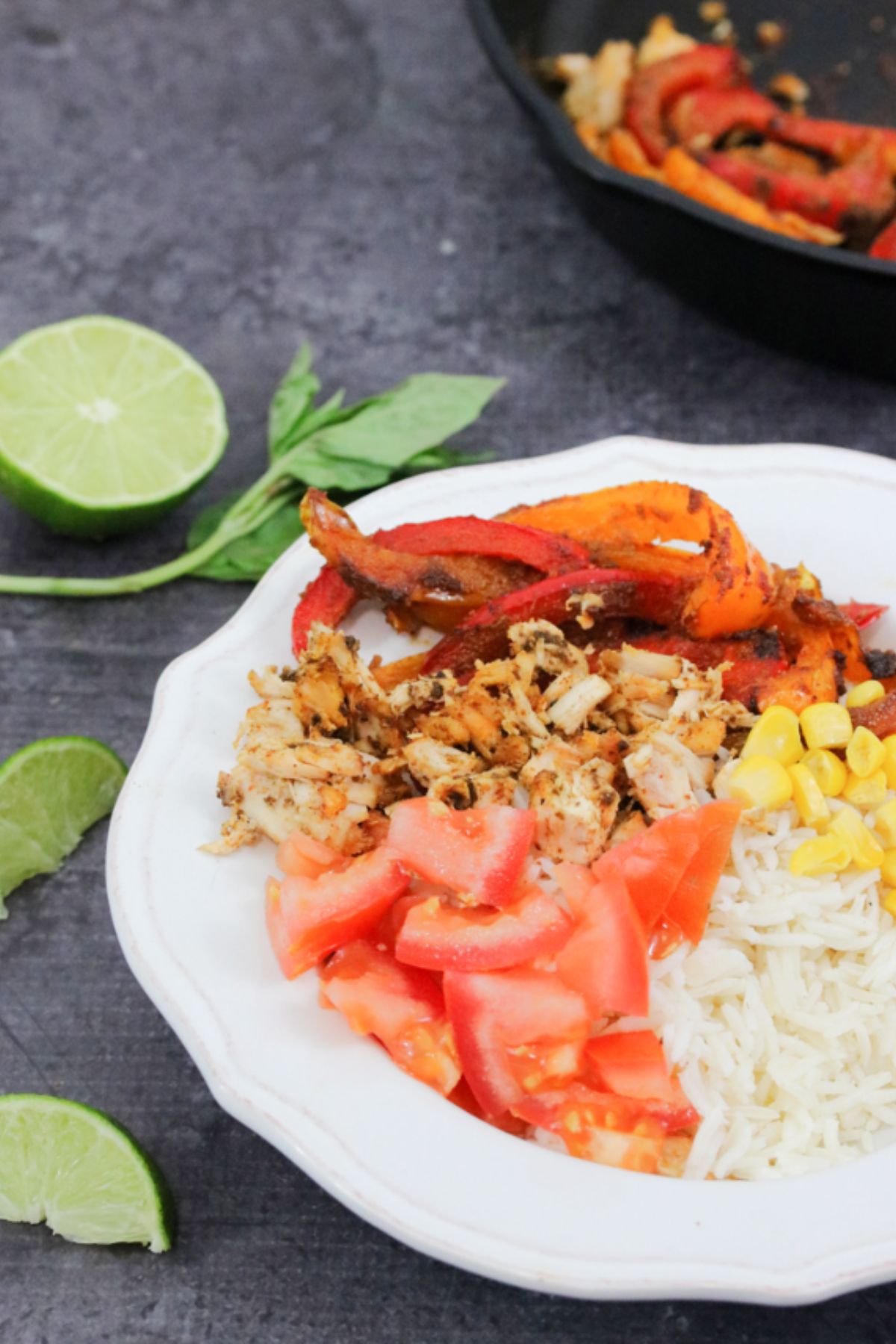 Chicken fajita bowl on rice with tomatoes and peppers in a white bowl with lime on the side.