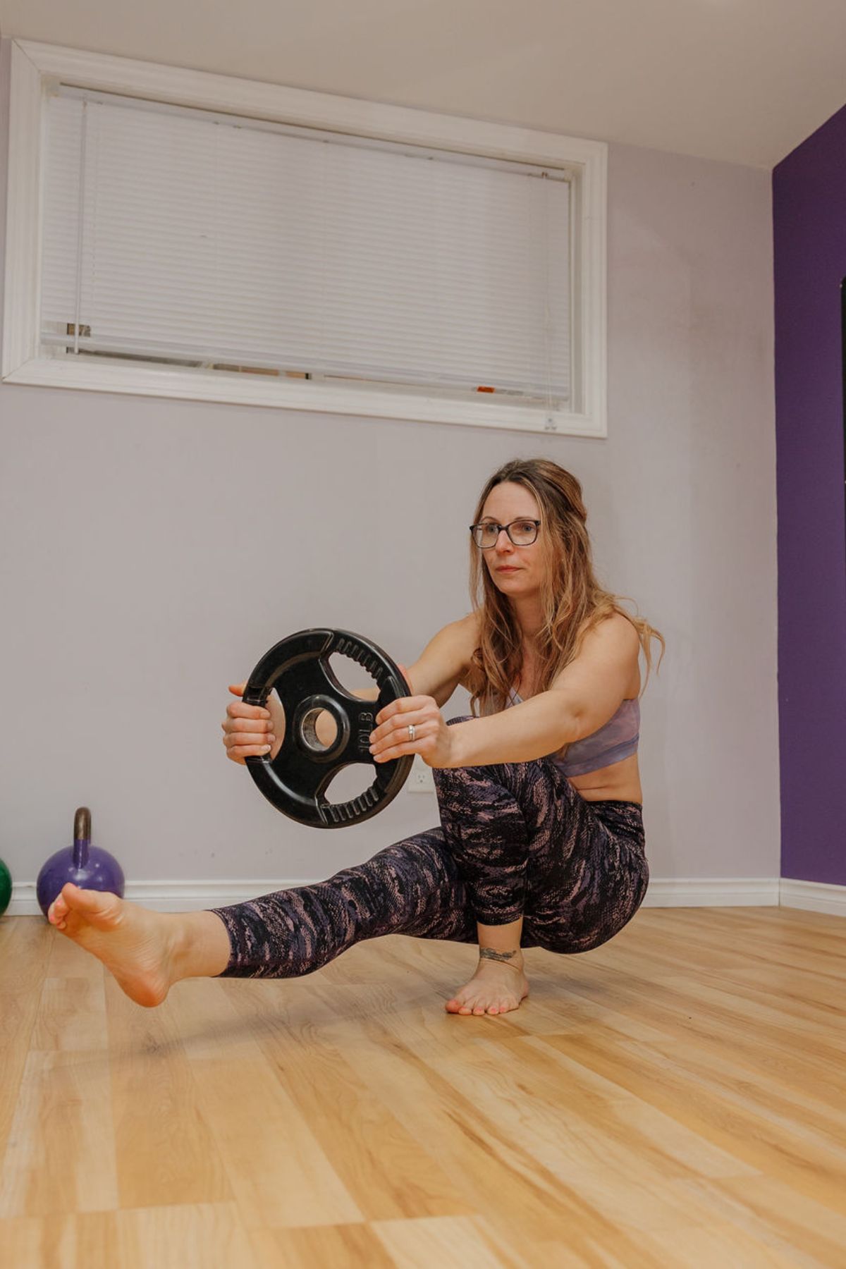 Woman in a single leg squat holding a weight plate.