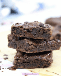Three gluten-free chocolate brownie squares stacked with a faint image of brownies and milk behind them