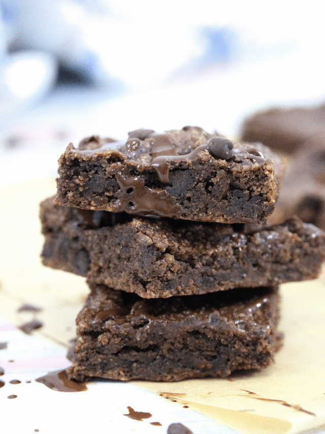 Three gluten-free chocolate brownie squares stacked with a faint image of brownies and milk behind them