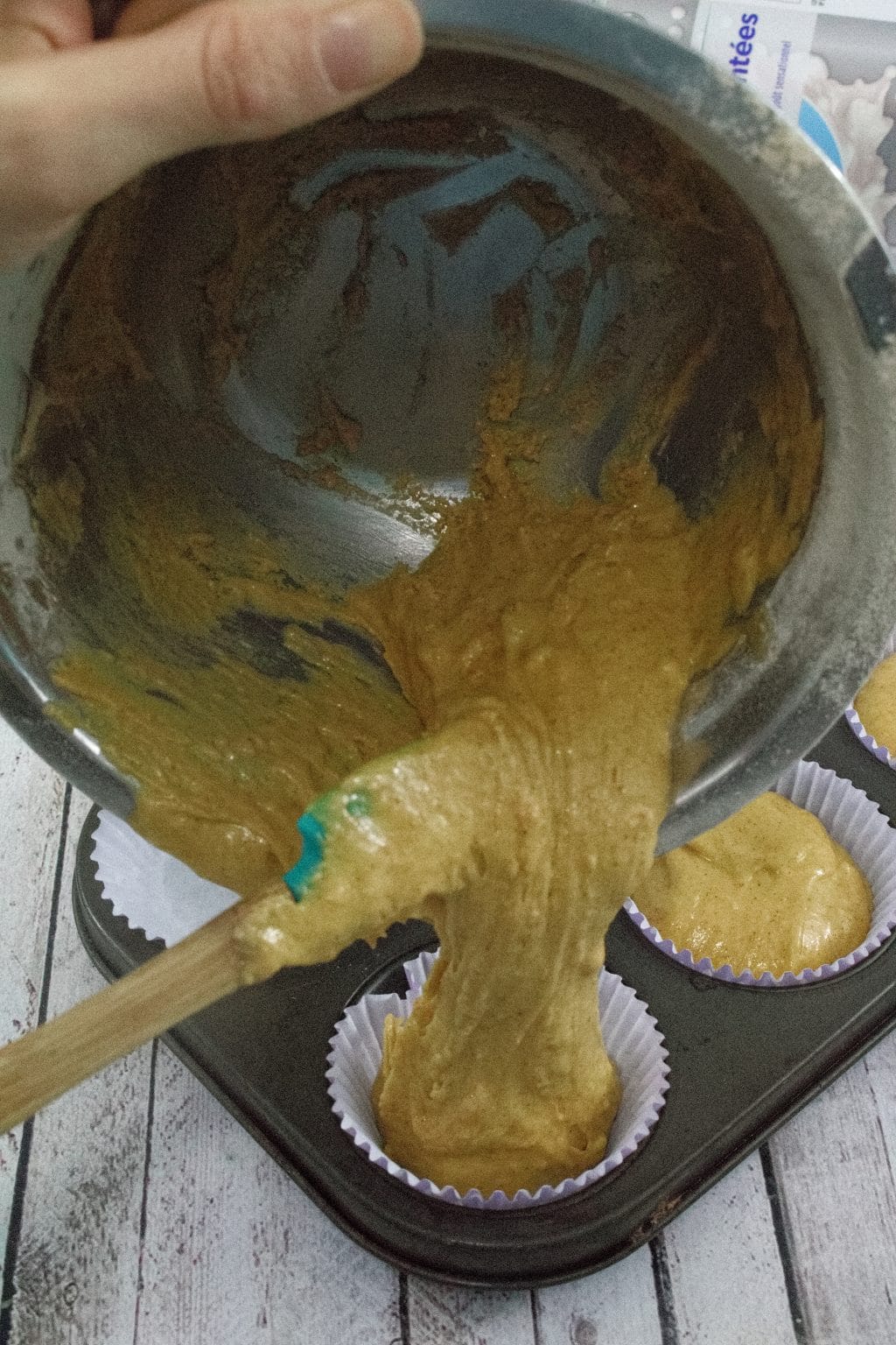 Muffin batter being poured from a steel bowl into a lined muffin tray