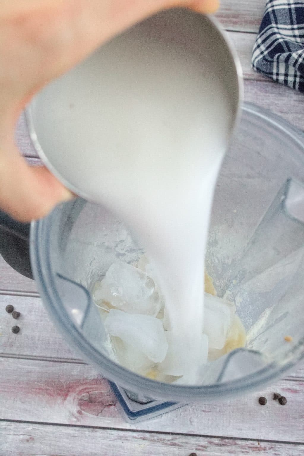 Hemp milk being poured into a blender with protein powder and ice cubes