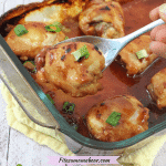 Cooked teriyaki chicken thighs in sauce in a glass baking tray with green onions on top and a spoon holding one chicken thigh up from the tray