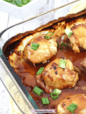 oven baked teriyaki chicken thighs in a blass baking tray covered in gluten-free sauce with green onions on top