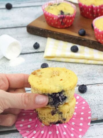 Blueberry muffins stacked on another muffin on a pink muffin liner with more muffins behind them.