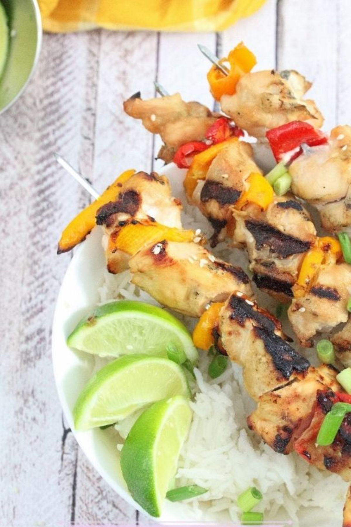 Three teriyaki chicken skewers on a bed of rice in a white bowl with limes on it and a bowl of limes beside it.