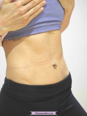 Pin image with text: close up shot of a woman in purple sports bra and black pants lifting her shirt to show a flat tummy