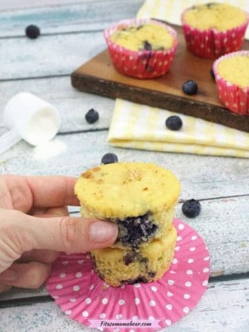Blueberry muffins stacked on another muffin on a pink muffin liner with more muffins behind them.