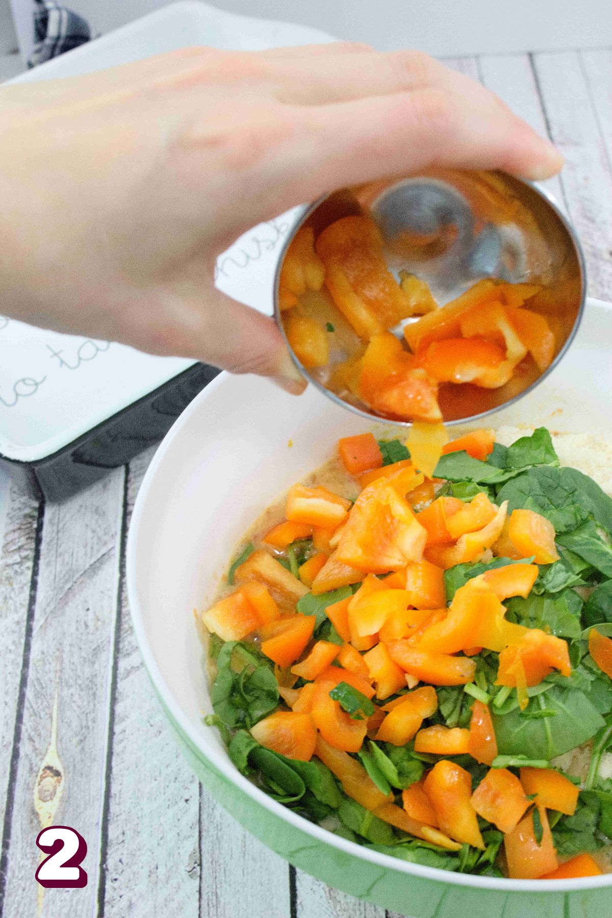 Orange peppers being poured into a bowl of eggs and spinach.