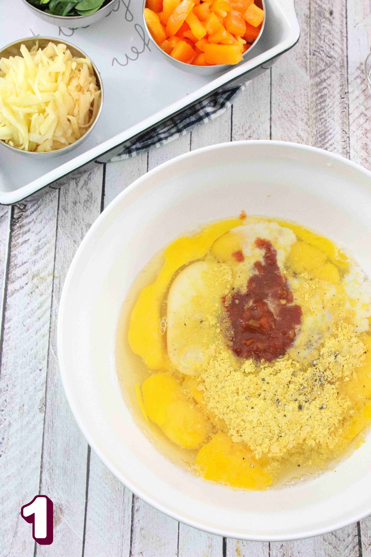 Eggs, nutritional yeast. and salsa in a mixing bowl with ingredients in measuring cups behind it.
