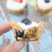 a close up image of two fingers holding a granola cup with yogurt and blueberry on top and the cup has been bitten in half