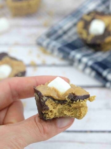 Peanut butter s'mores cup with a marshmallow on top held between two fingers with more smores cups behind it.