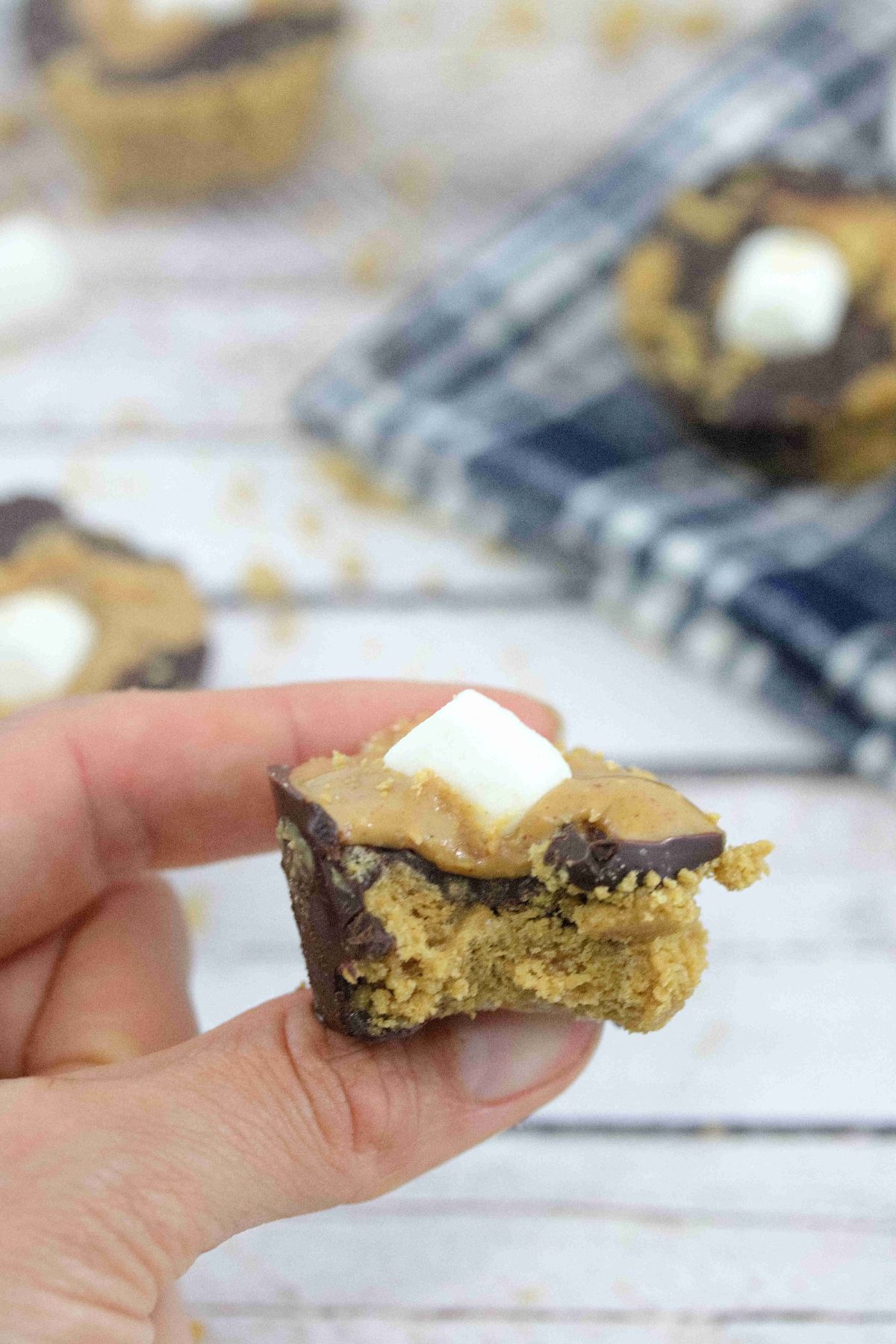 Peanut butter s'mores cup with a marshmallow on top held between two fingers with more smores cups behind it.