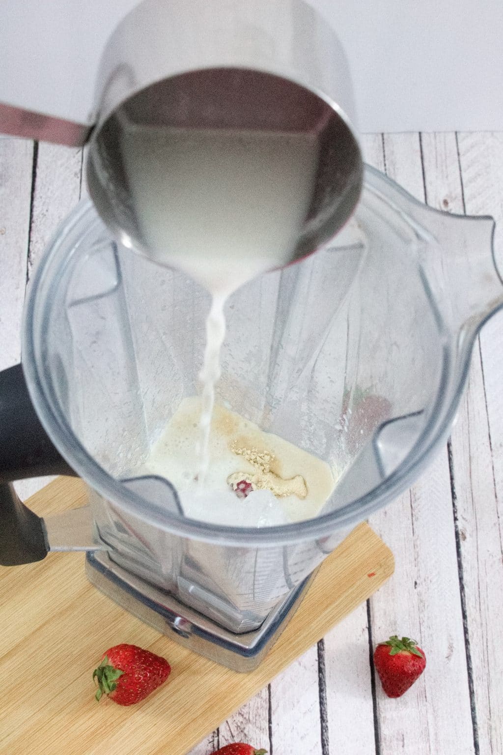 Blender on a cutting board with milk being poured on top