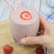 Strawberry protein shake on a wooden cutting board with berries around it.