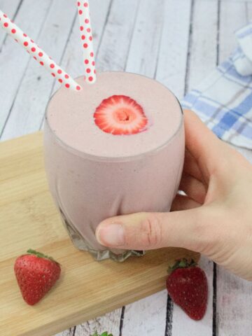 Strawberry protein shake on a wooden cutting board with berries around it.