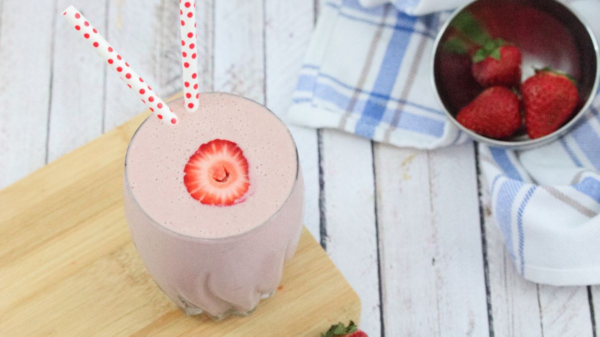 Strawberry protein shake in a glass on a cutting board with strawberries around and behind it