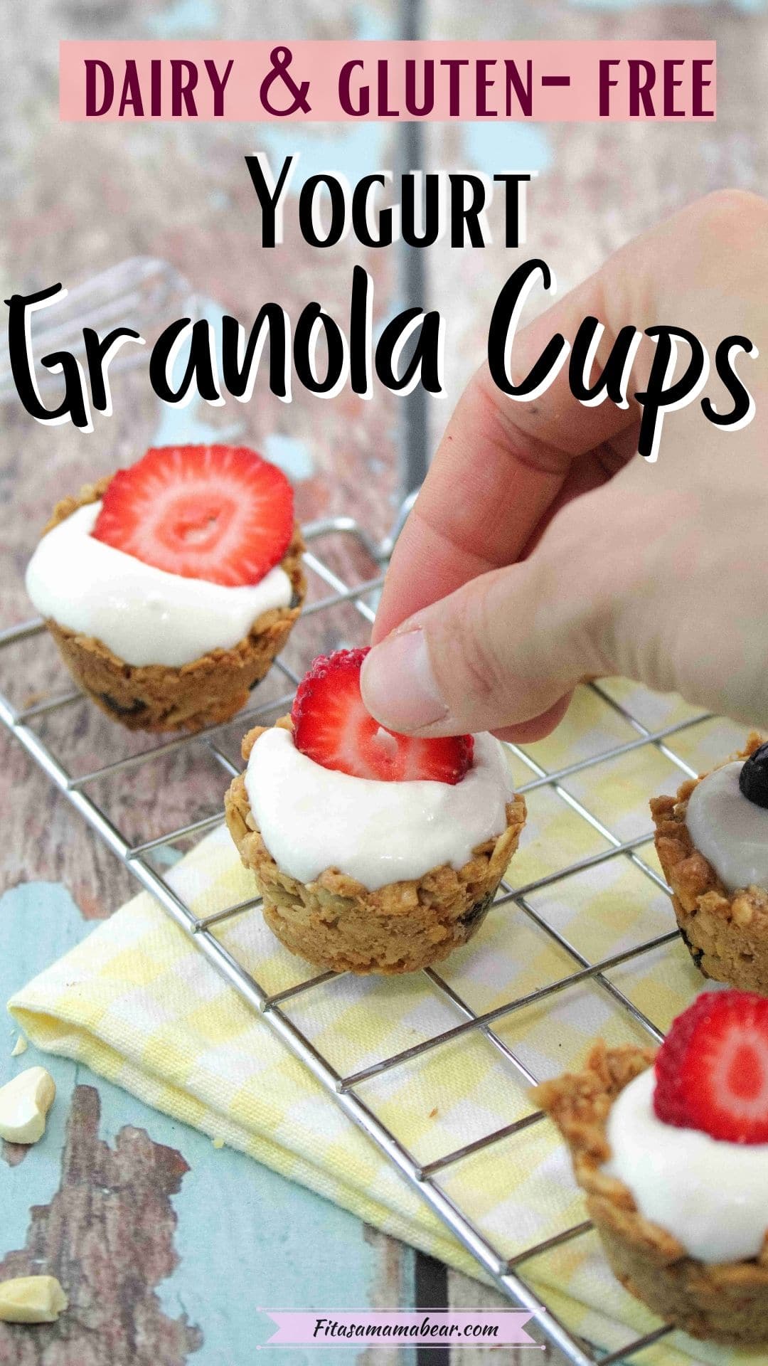 Pin image with text: A hand placing a slice if strawberry onto a granla cup with yogurt on top on a cooling rack with a yellow linen under it
