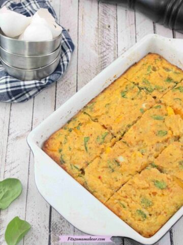 Dairy-free egg casserole baked in a pan with spinach around it and a blue linen with tin cups and egg shells behind it