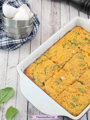 Dairy-free egg casserole baked in a pan with spinach around it and a blue linen with tin cups and egg shells behind it