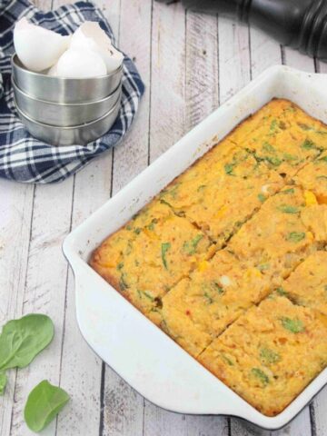 Dairy-free egg casserole baked in a pan with spinach around it and a blue linen with tin cups and egg shells behind it