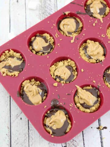 Graham cracker crust with chocolate and peanut butter on top in a mini, silicone red muffin tin