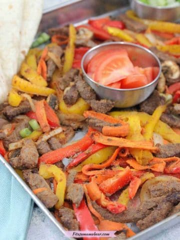 Sheet pan steak fajitas with red and yellow peppers with a tin of tomatoes on the sheet pan.