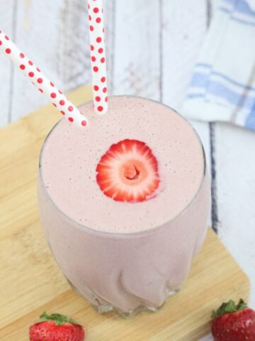 Strawberry protein shake in a glass on a cutting board with strawberries around and behind it
