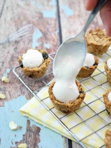 A spoonful of yogurt being dalloped onto mini granola cups on a cooling rack with a yellow linen under it