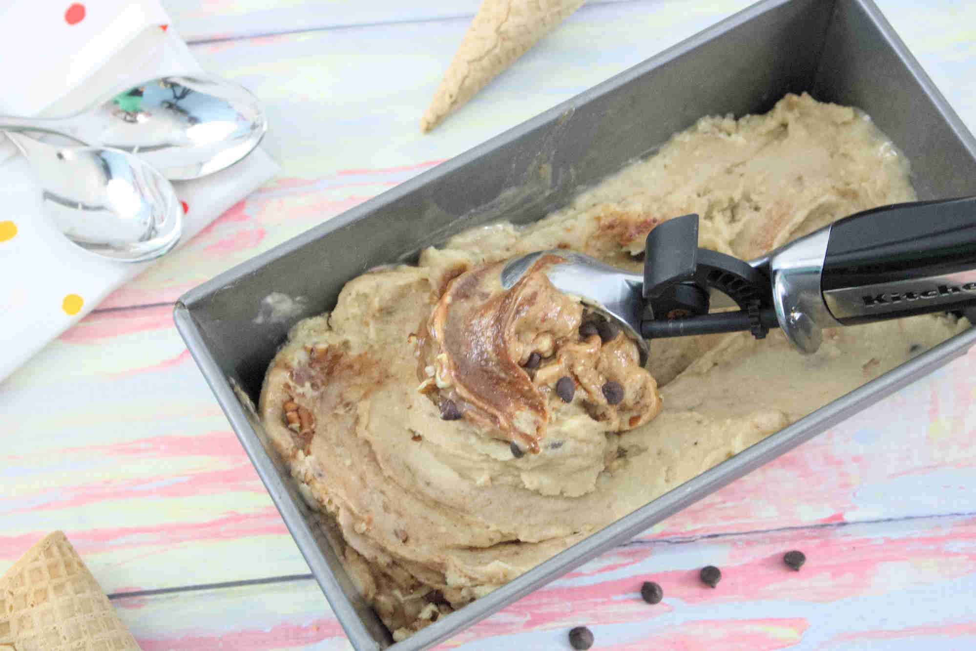 Pin image with text: a steel baking loaf with protein ice cream swirled with chocolate and an ice cream scoop in it with ice cream cones around the pan