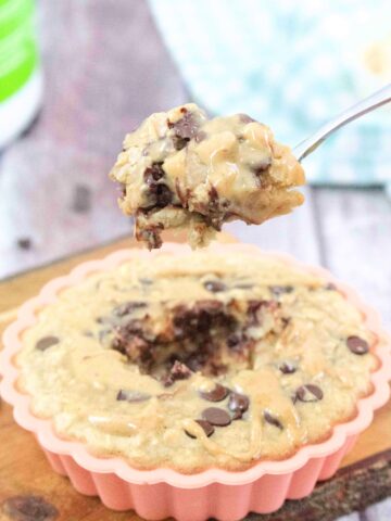 Orange silicone mold on a cutting board with peanut butter chocolate chip baked oatmeal with a spoonful coming out and a blue linen behind it.