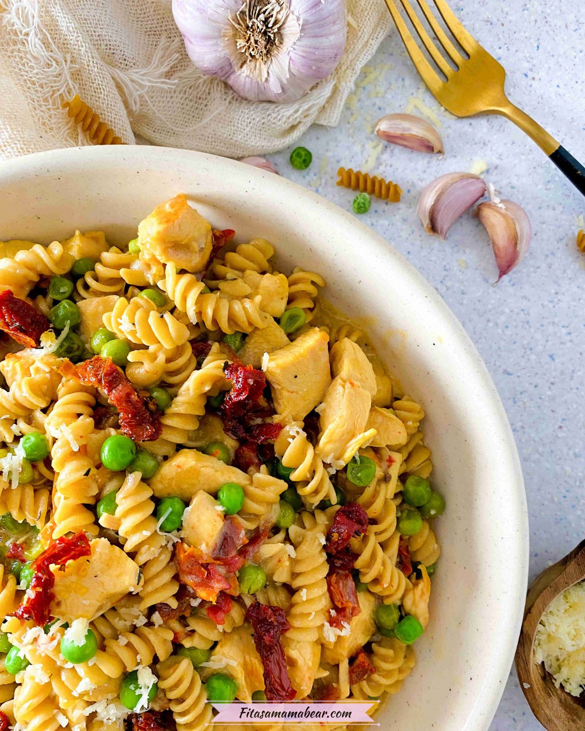 white bowl with chicken pasta with sundried tomatoes and peas and garlic and a light linen around the bowl