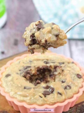 orange solicone mold on a cutting board with peanut butter chocolate chip baked oatmeal with a spoonful coming out and a blue linen behind it