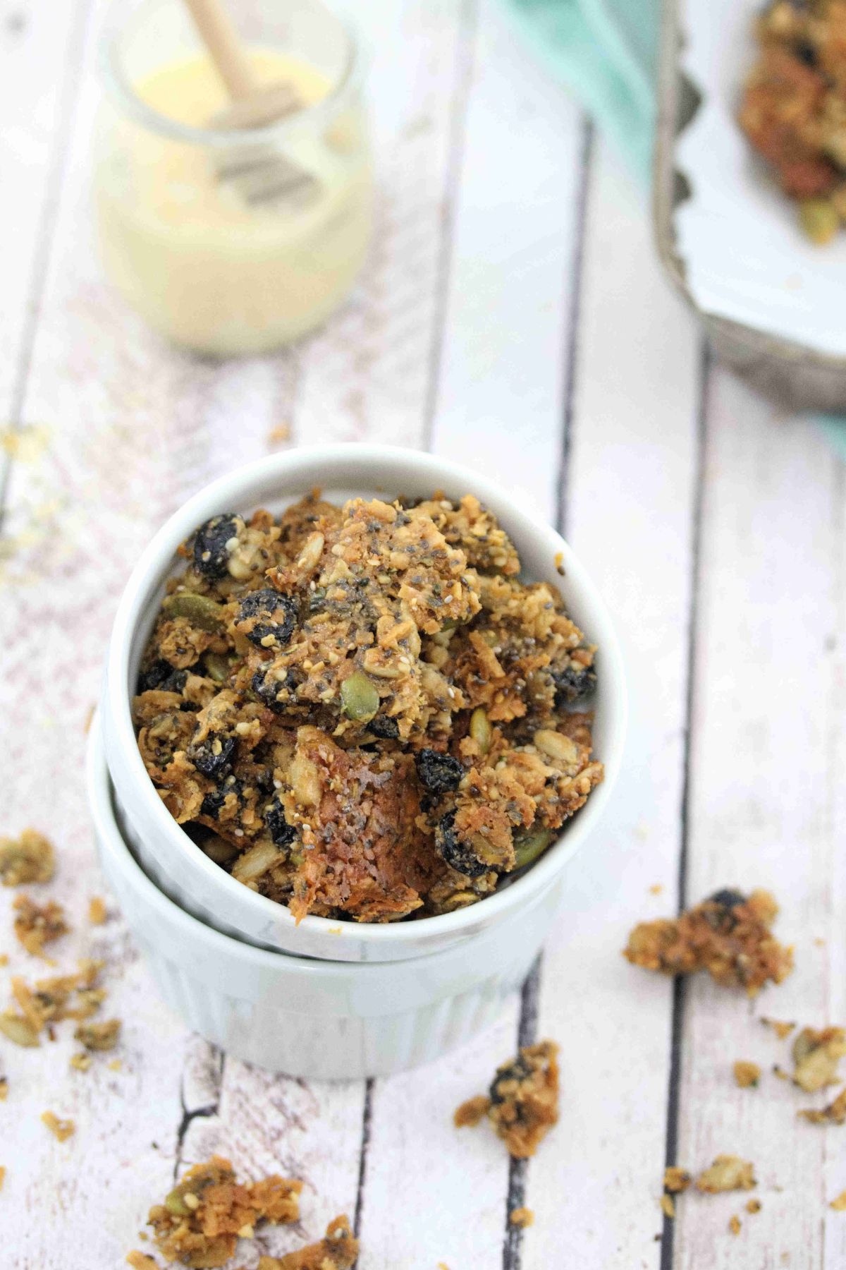 two white ramekins stacked and the top one full of nut-free granola with more granola around the bowls and on a baking tray behind them.