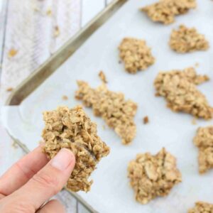 Baking sheet lined with parchment paper with granola clusters on it and a hand holding on cluster close up