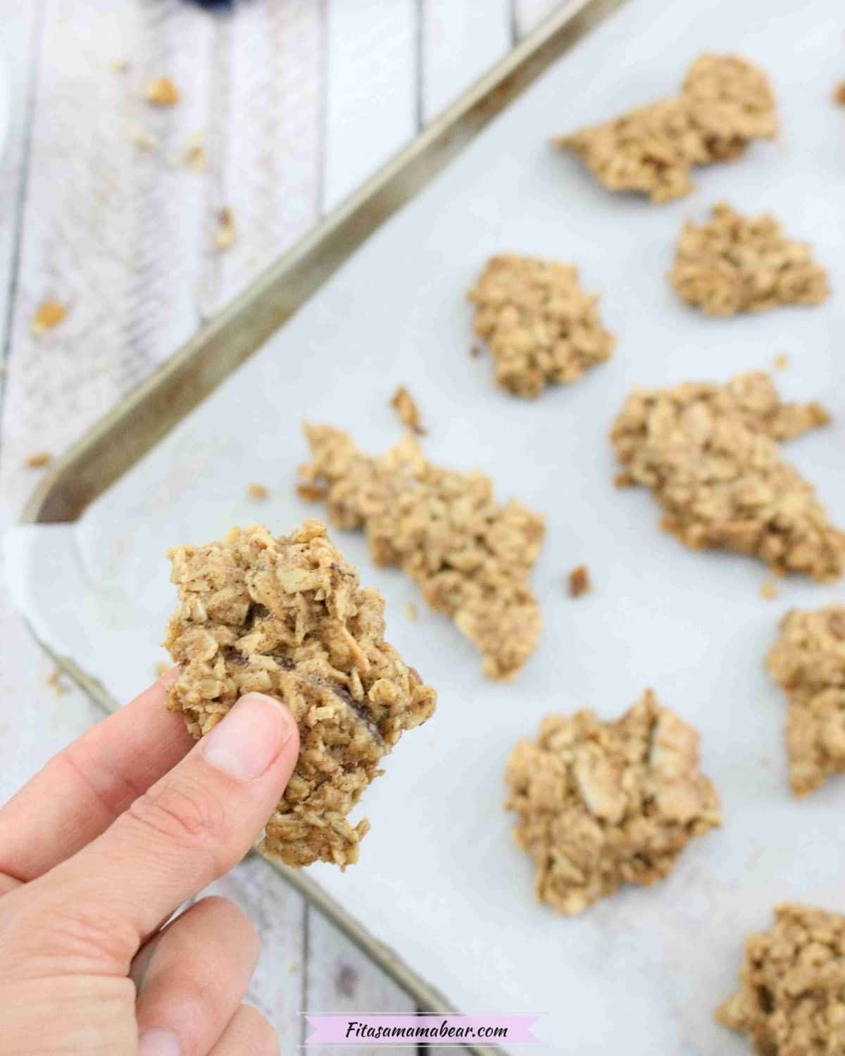 Baking sheet lined with parchment paper with granola clusters on it and a hand holding on cluster close up
