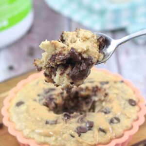 orange solicone mold on a cutting board with peanut butter chocolate chip baked oatmeal with a spoonful coming out and a blue linen behind it
