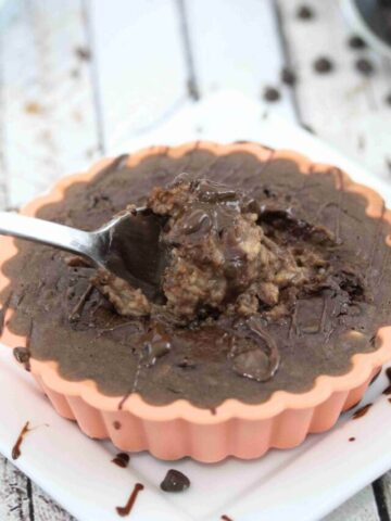 orange mold on a white plate with chocolate protein baked oats and a spoon in the oats with chocolate chips around it