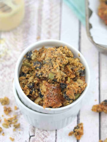 two white ramekins stacked and the top one full of nut-free granola with more granola around the bowls and on a baking tray behind them