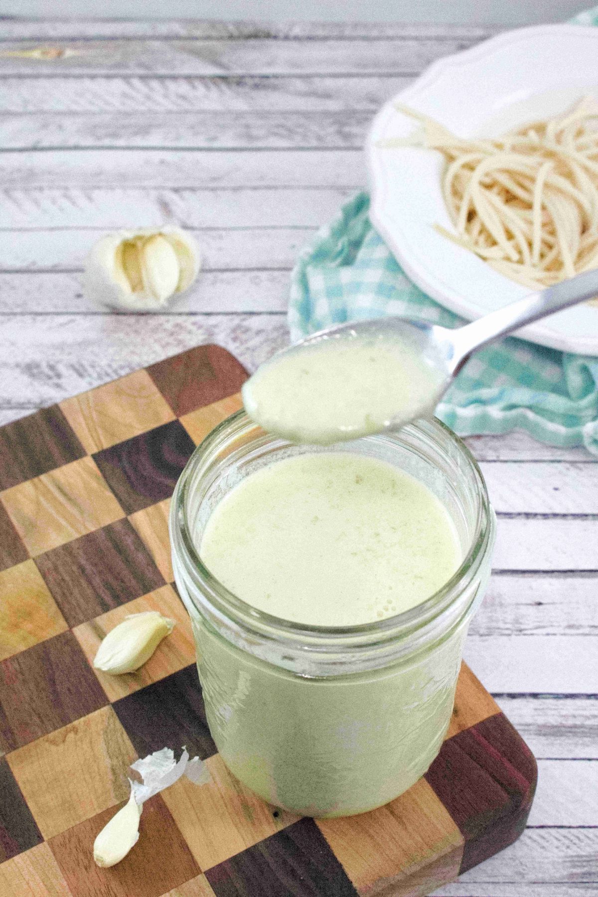 Dairy free alfredo sauce in a mason jar with a spoon pulling out and the jar on a checkered wooden cutting board.